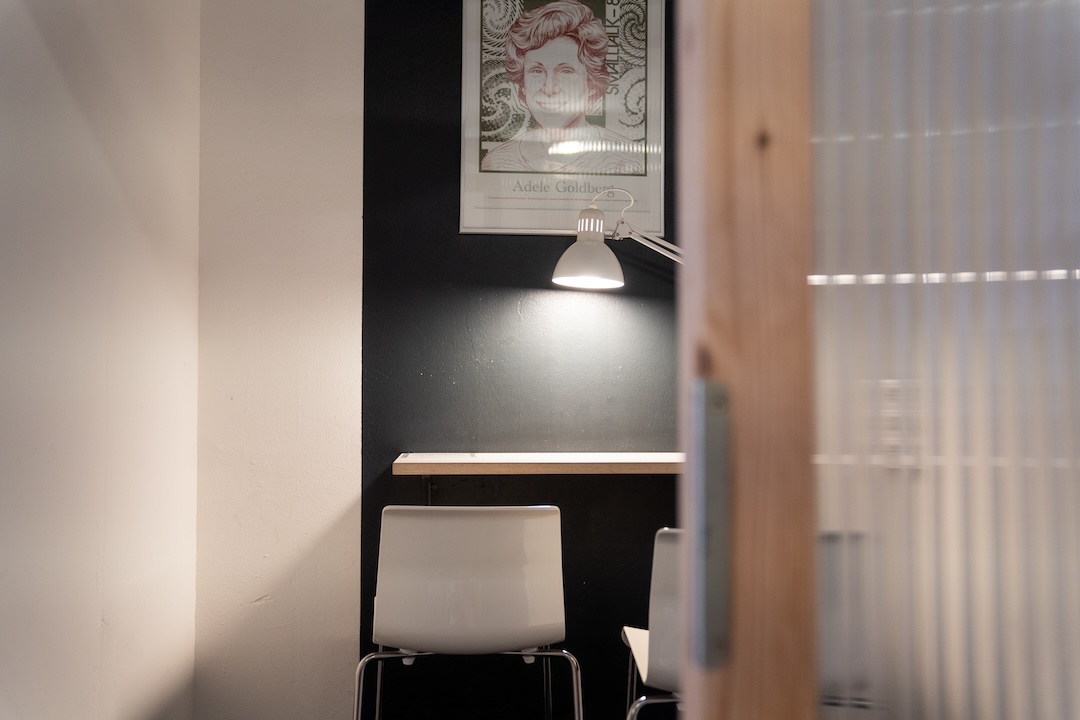 Im Open Space bieten wir für unsere Coworker außerdem Telefonkabinen an, in denen sie ungestört telefonieren können Blick in eine Telefonkabine mit Hochtisch, Licht und halbtransparenter Wand